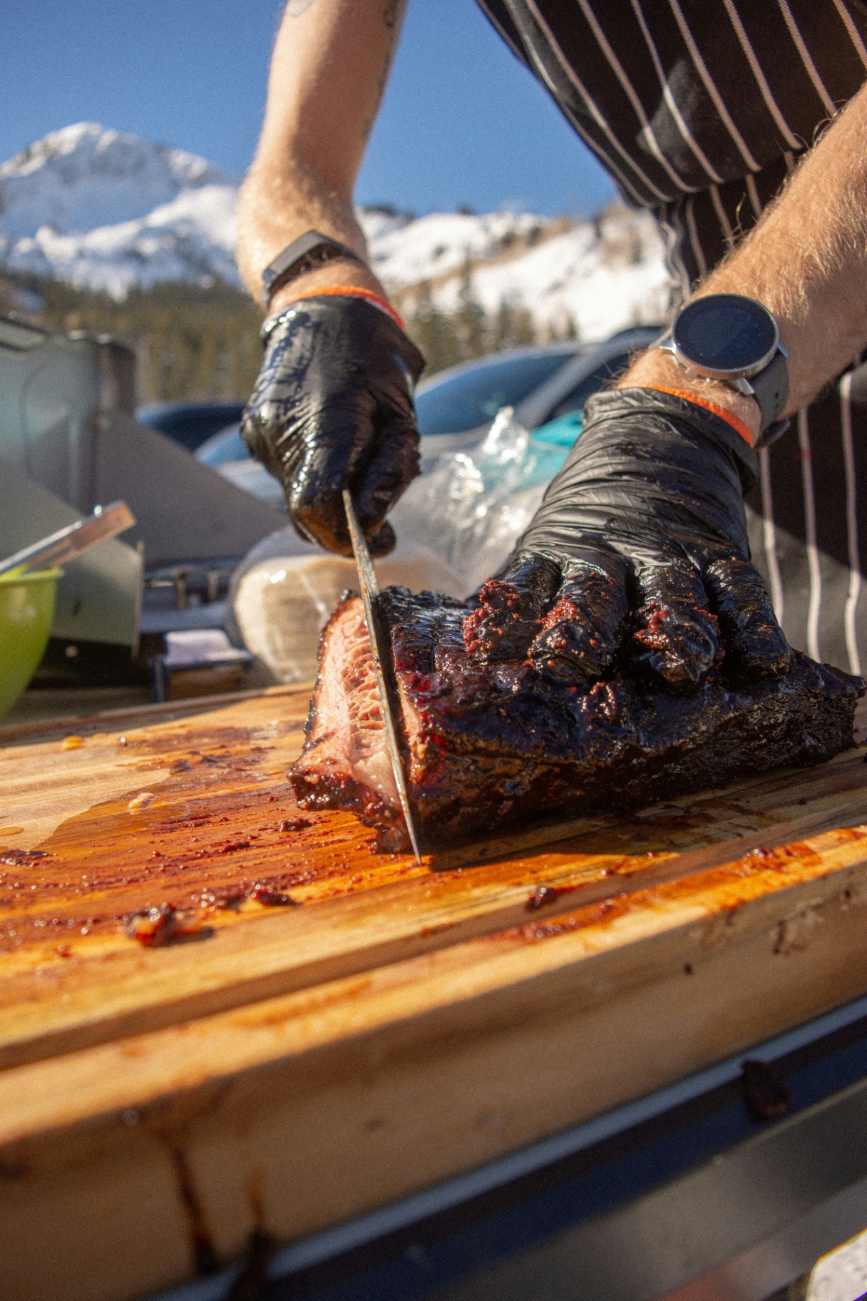 Chef slicing smoked brisket against snowy Colorado peaks